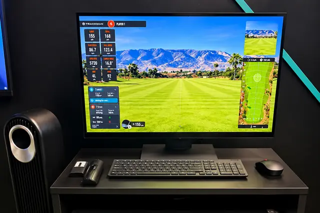 A Trackman screen showing a fairway view and shot numbers, above the black Trackman cabinet.
