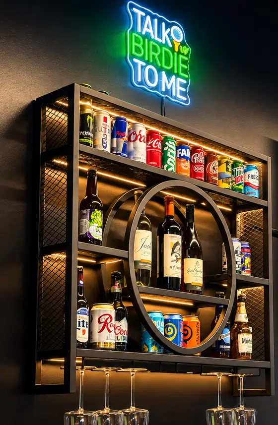A neon sign reading Talk Birdie to Me above a lit shelf of soft drinks, wine and beer.
